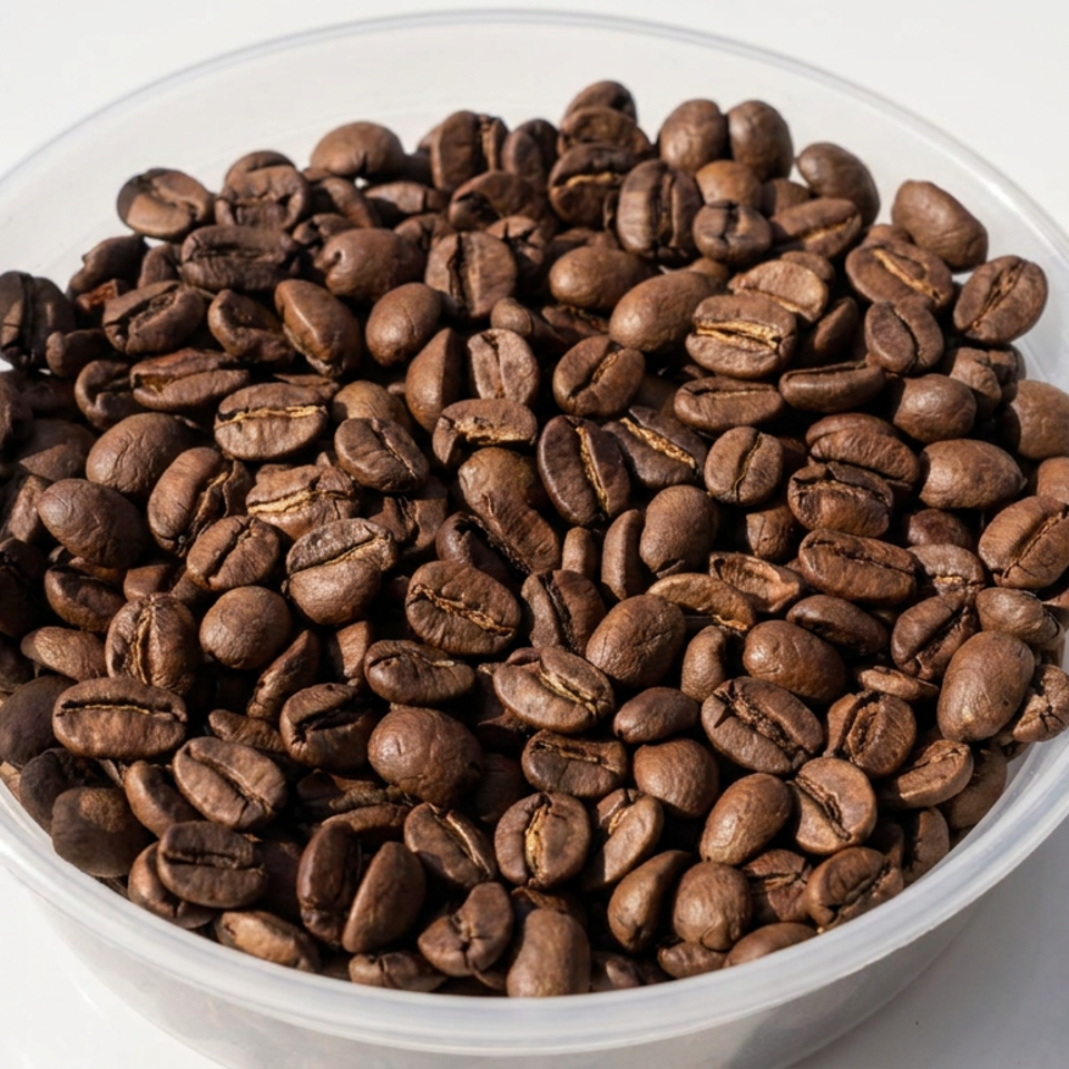 Bowl filled with roasted coffee beans on a white surface, illuminated by strong sunlight.